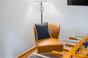 A room with a brown leather chair, a dark cushion, a wooden floor, and a foosball table. - Story Time Retreat (Nashville)