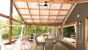 A covered outdoor deck with a hammock, a table with chairs, and a grill.