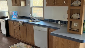 A compact kitchen with wooden cabinets, a dishwasher, and a countertop with a dish rack.