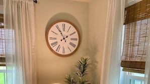 Een woonkamer met een ronde wandklok, een lamp, een potplant en twee banken met blauwe kussens.