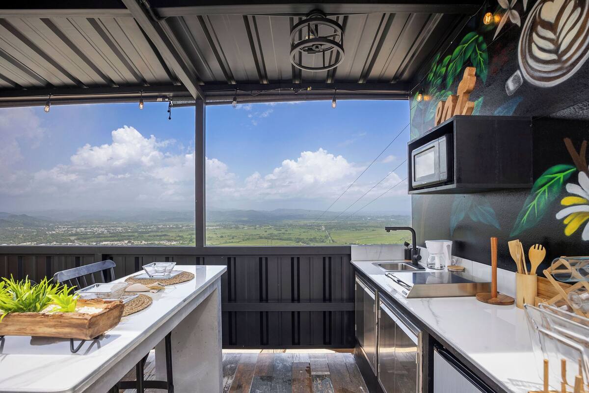 A modern kitchen with a view of the countryside, a wooden plant pot, and a microwave.