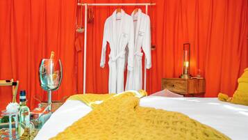 A hotel room with a bed, a bedside table, a lamp, and two white robes hanging on a rack.