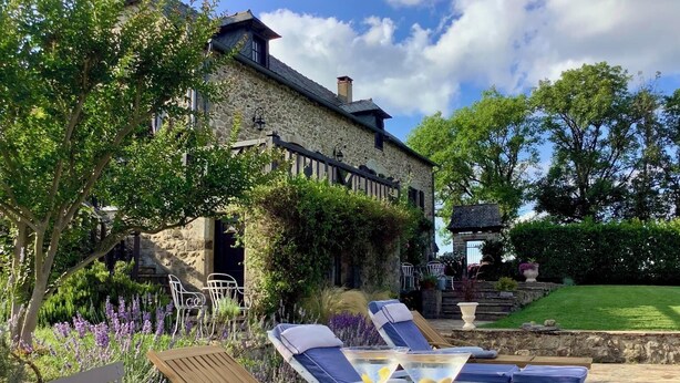 Edificio de piedra con un patio jardín que tiene sillones de descanso y una mesa con bebidas.