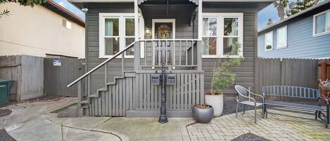 A two-story house with a porch, a staircase, a potted plant, and a bench.