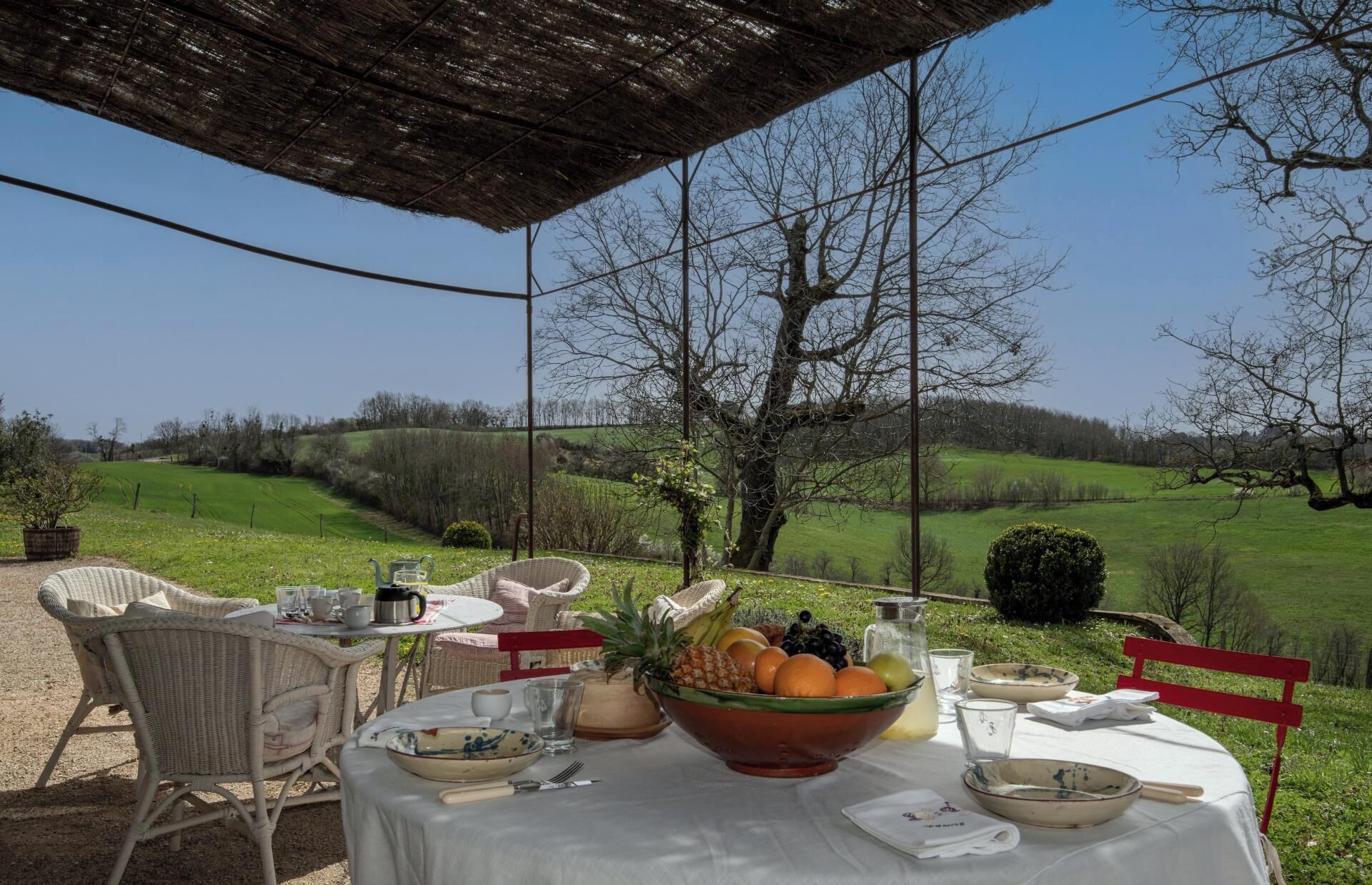 Un espace de restauration en plein air, avec des chaises en osier et une table dressée pour un repas, offrant une vue sur un paysage verdoyant.