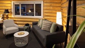 A cozy room with a wooden log wall, a sofa with cushions, a patterned armchair, a round side table, and a window with blinds. - River's Edge Retreat (Clearwater)