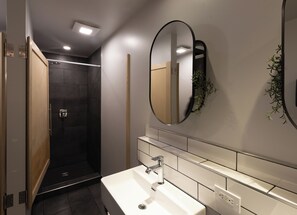 A modern bathroom with a white sink, a mirror, and a shower area.