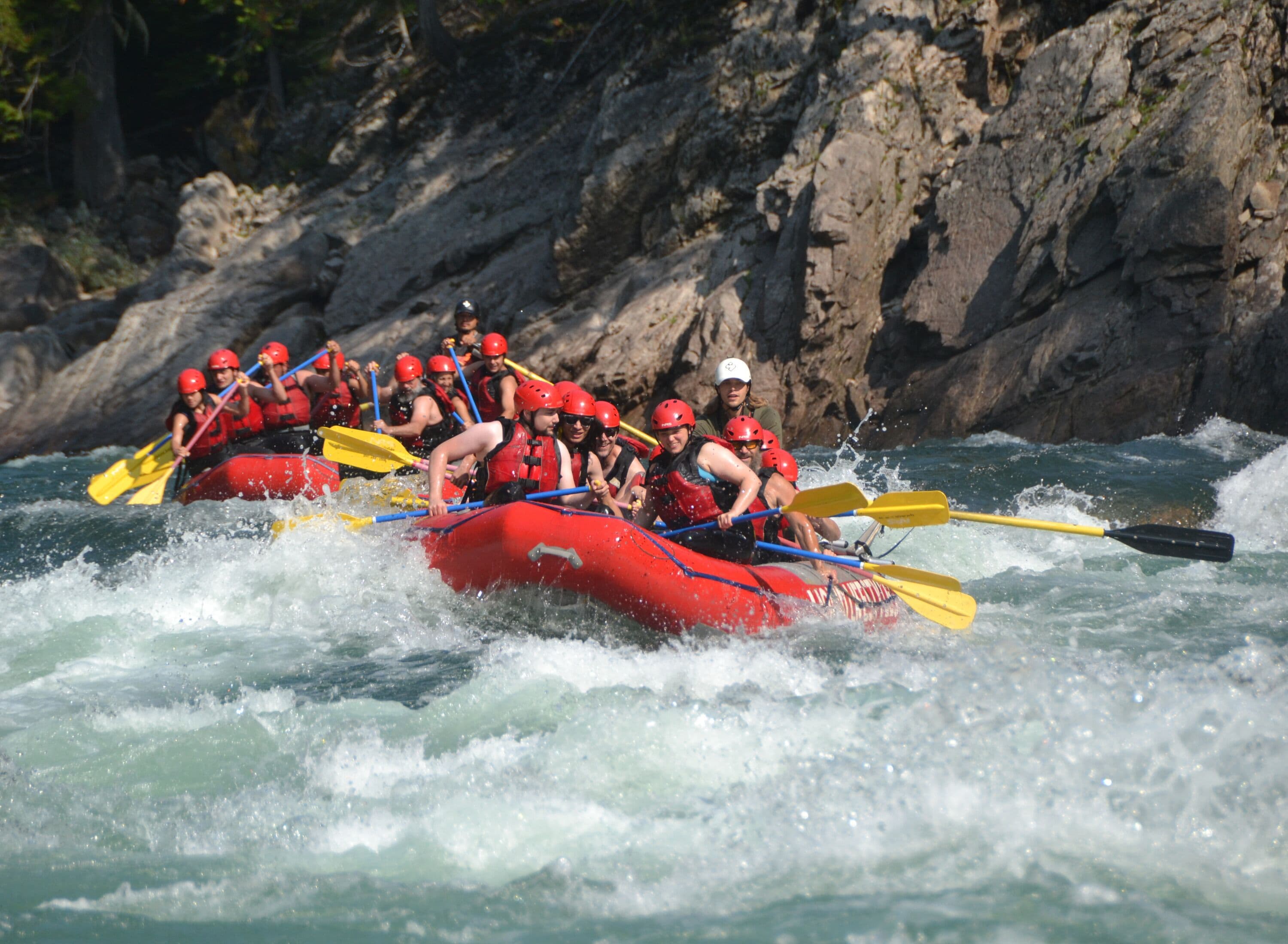 Un groupe de personnes à bord d’un radeau rouge navigue sur une rivière à courant rapide.