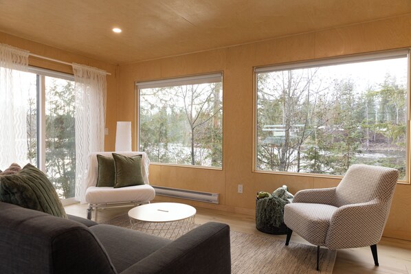 A modern living room with large windows, a sofa, a chair, and a coffee table.