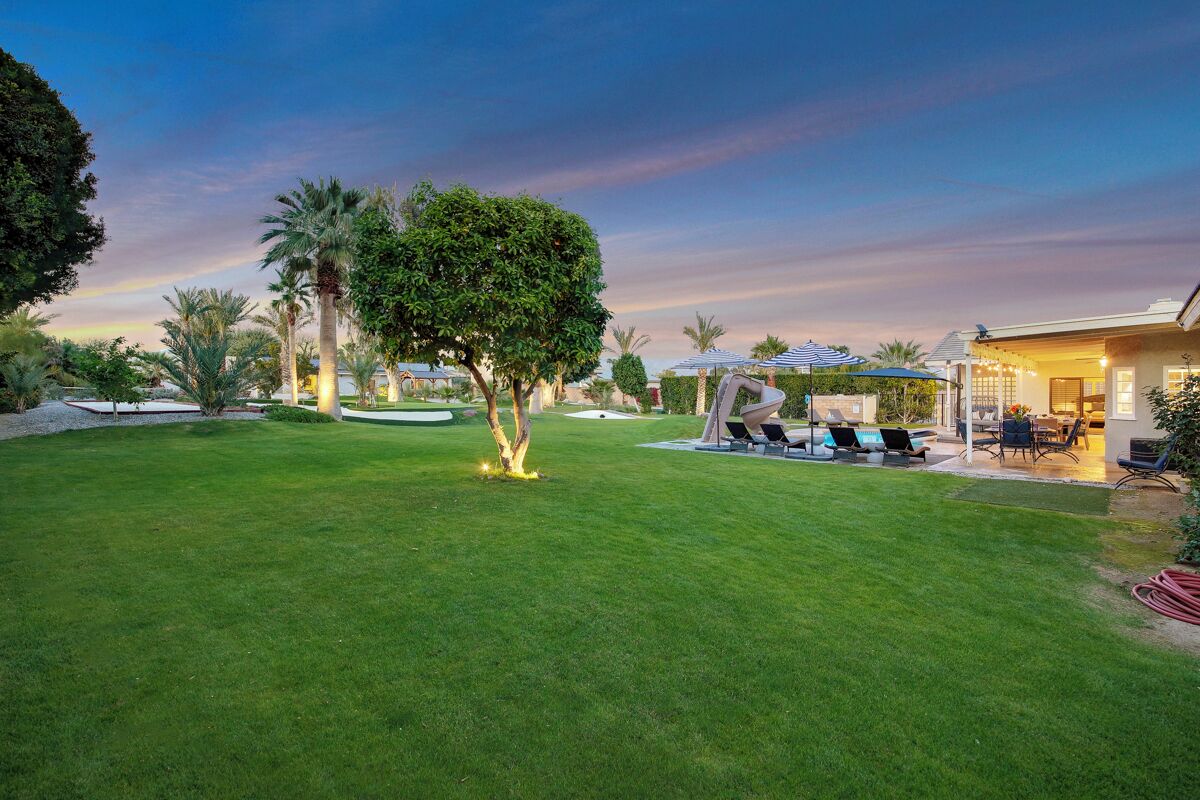 A well-maintained lawn with a tree, outdoor seating area, and a building with a covered patio.