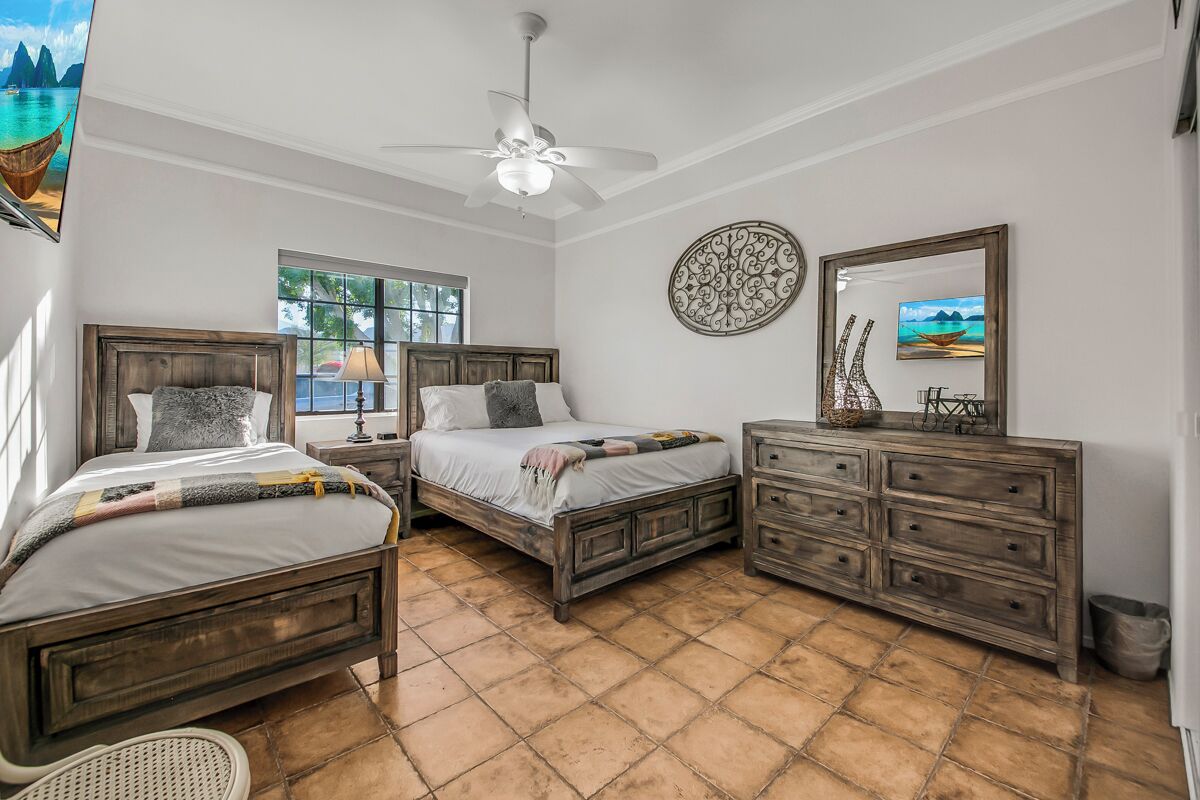 A bedroom with two wooden beds, a ceiling fan, a dresser, and a window with a view of the ocean.