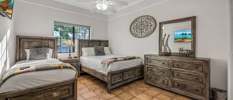 A bedroom with two wooden beds, a ceiling fan, a dresser, and a window with a view of the ocean.