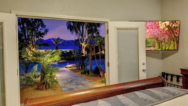 Un dormitorio con vista a un jardín ajardinado y a una playa al atardecer.