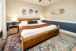 Une chambre à coucher avec un lit en bois, deux tables de chevet, un grand miroir et des œuvres d’art florales accrochées au mur.