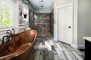 A bathroom with a vintage copper bathtub, a shower area with a glass door, and a white door.