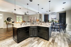 A modern kitchen with dark cabinetry, a marble countertop, and a dining area with a table and chairs.