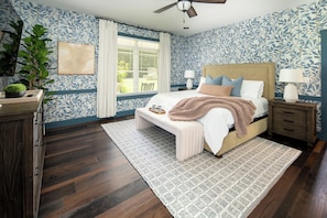 A bedroom with a bed, bedside tables, a nightstand, a ceiling fan, a window with blinds, and a potted plant.