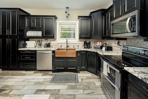 A modern kitchen with dark cabinetry, a stainless steel range, and a window with blinds.