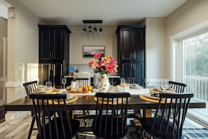 A dining area with a table set for six, surrounded by black chairs, with a vase of flowers in the center. - Modern Forest Escape w/ Pickleball, Hot Tub, Sauna, Gym, Fire Pit & Gameroom! (Mars Hill)