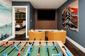 A room with a foosball table, a television mounted on the wall, and a painting. - Modern Forest Escape w/ Pickleball, Hot Tub, Sauna, Gym, Fire Pit & Gameroom! (Mars Hill)