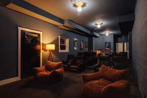 A home theater room with a dark carpet, leather recliners, a lamp, framed movie posters, and a door.