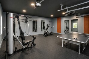 A gym with exercise equipment, a ping pong table, and mirrors on the walls.