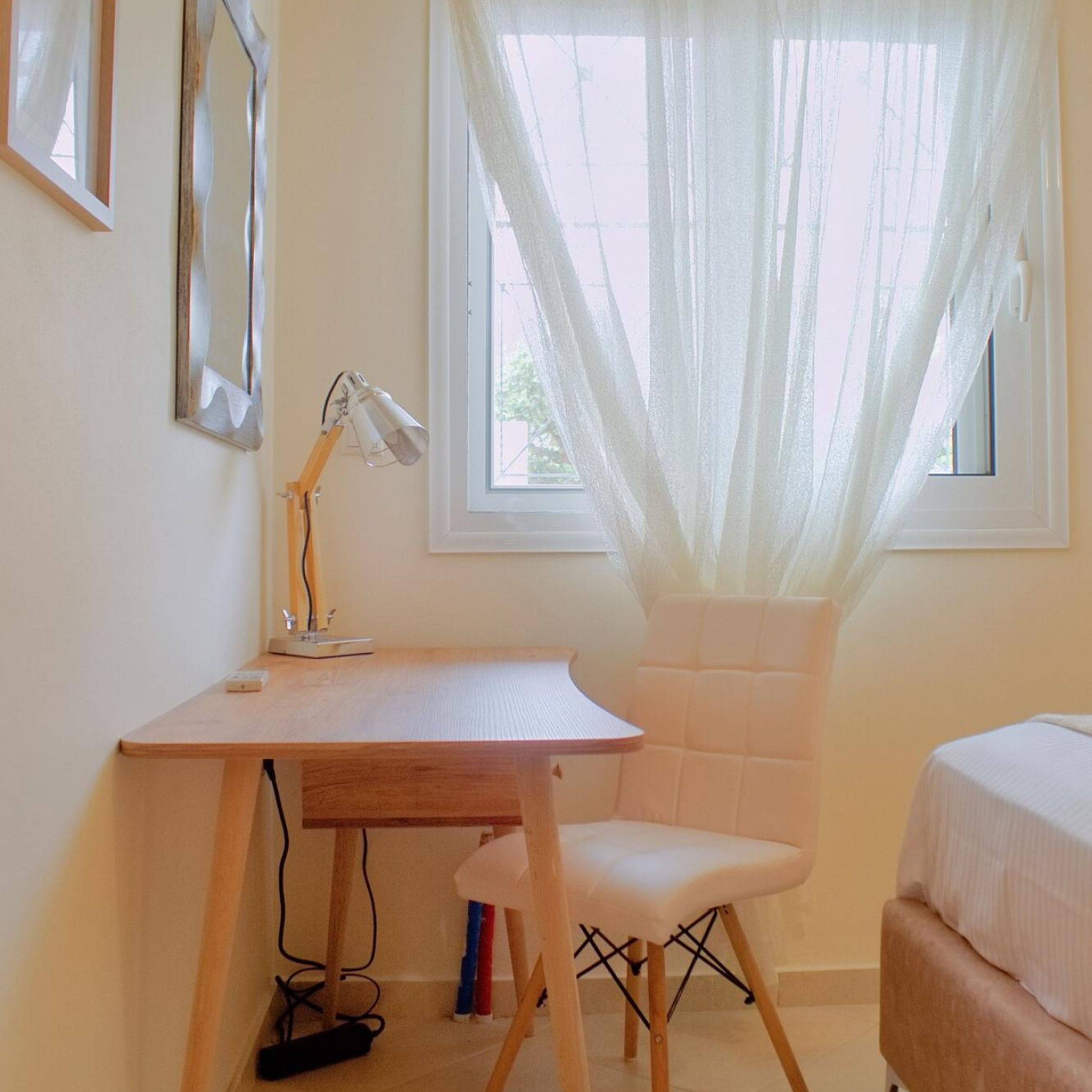 A room with a wooden desk, a white chair, a lamp, and a window with sheer curtains.