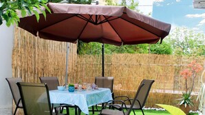 An outdoor patio with a table and chairs, a brown umbrella, and a bamboo fence in the background. - D A Sea Breeze Next to the sea (Kalamata)