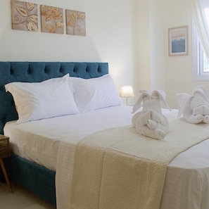 Una habitación de hotel con una cama grande, ropa de cama blanca, un cabecero azul y dos obras de arte colgadas en la pared.