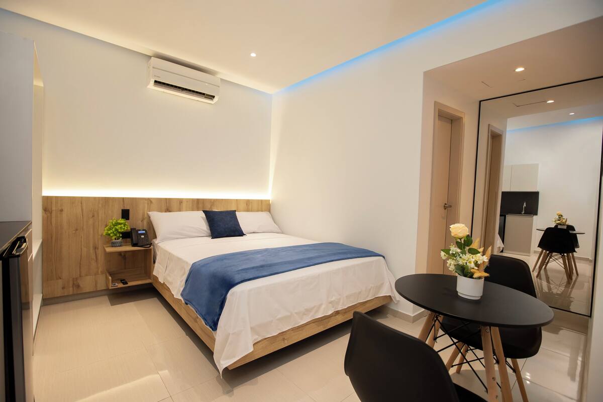 Ein modernes Hotelzimmer mit einem hölzernen Bett, einem Nachttisch mit Lampe, einem kleinen Tisch mit Blumenvase und einem schwarzen Stuhl.