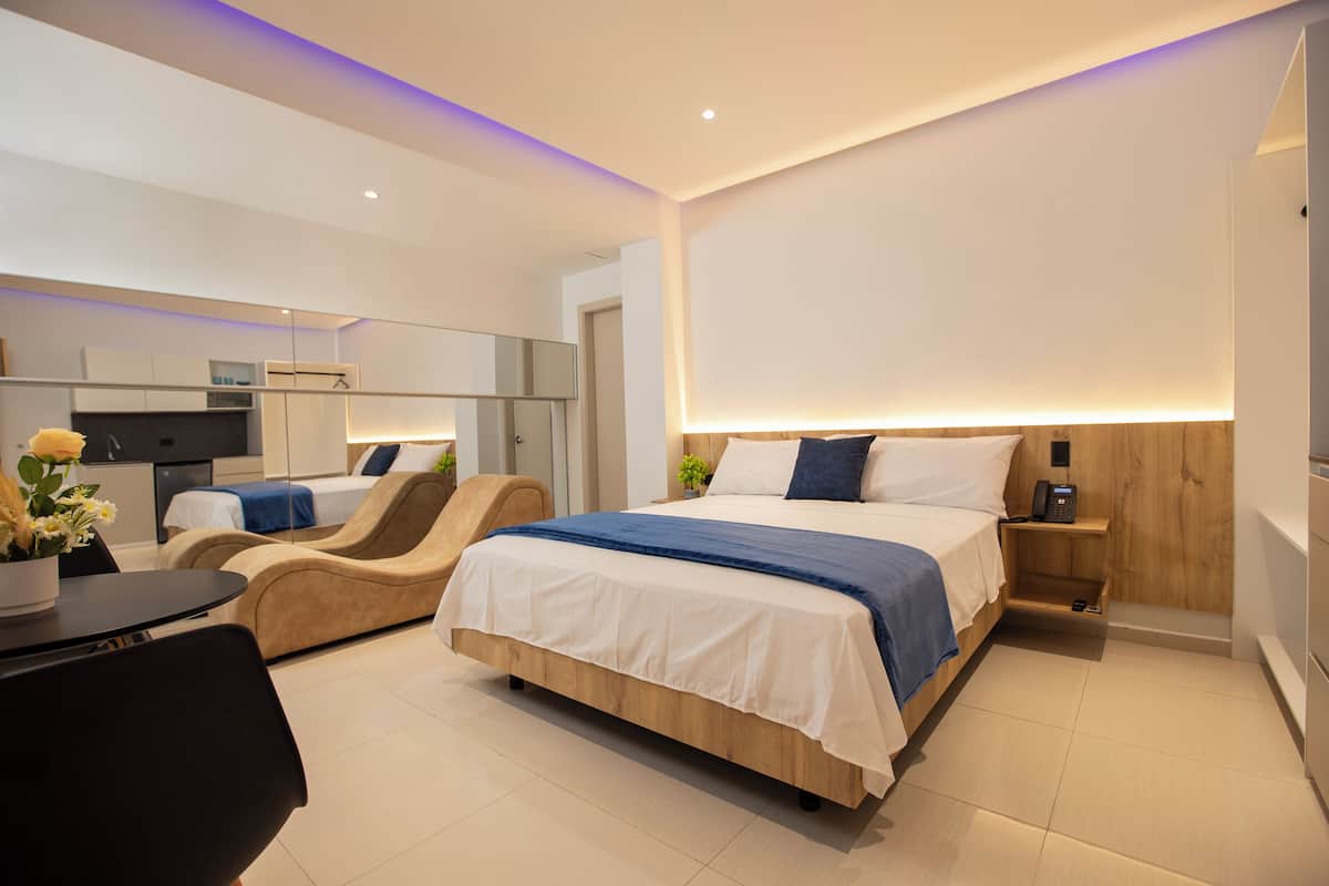 Ein modernes Hotelzimmer mit Bett, einer Sitzecke, einem Schreibtisch und einer Küchenzeile.
