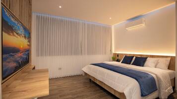 A modern hotel room with a large bed, a wooden desk, a wall-mounted air conditioner, and a large window with sheer curtains.