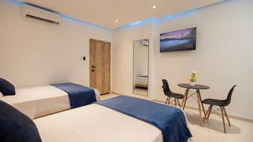 Habitación de hotel con dos camas, una puerta de madera, televisión, espejo y una pequeña mesa con sillas.