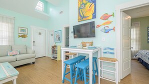 A cozy room with a teal wall, a white sofa, a dining table with blue stools, and a TV. - Perfect Family Fun  | Pool, King Bed+BBQ+Sleeps 6 (Rockport)
