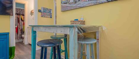 Une cuisine avec une table et des tabourets, un tableau accroché au mur et une porte donnant sur une autre pièce.