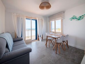 A modern living room with a grey sofa, a dining table with white chairs, and large windows with curtains. - R155 Beachfrontapartment 3 (Coma-ruga)