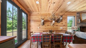 A wooden interior with a dining table set for four, flanked by two deer antlers on the wall, and a fireplace with a stone mantle.