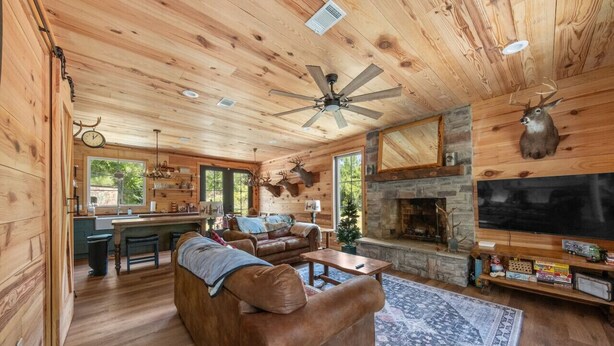 A log cabin interior with a fireplace, wooden ceiling, and mounted deer heads.