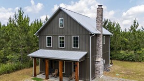A two-story house with a covered porch and a stone chimney.