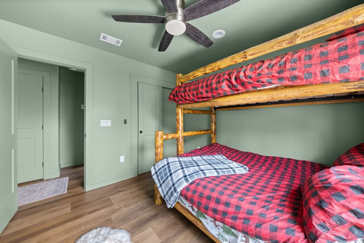 A bunk bed with red and black checkered bedding, a ceiling fan, and a wooden headboard.