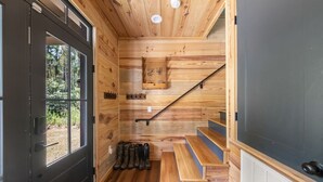 A wooden cabin interior with a staircase, a door leading outside, and a bench near the entrance.
