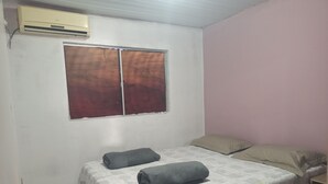 Ein Schlafzimmer mit einem Bett, zwei Kissen, einem Fenster mit Vorhang und einer Wandklimaanlage.