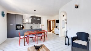 Una cocina moderna con armarios grises, un comedor con sillas rojas y una silla de mimbre en la sala.