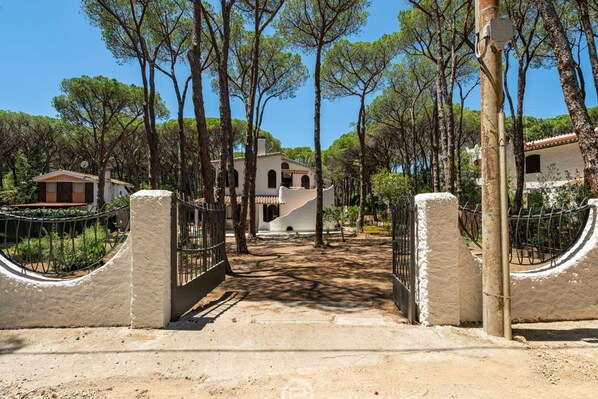 A gated entrance with a pathway leading to a building surrounded by trees.