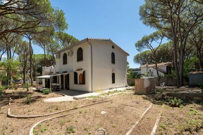 A two-story building with a tiled roof, a covered patio, and a garden with young trees and shrubs.