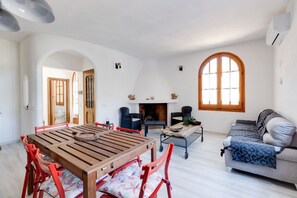 A spacious living area with a wooden dining table, red chairs, a sofa, and a fireplace.