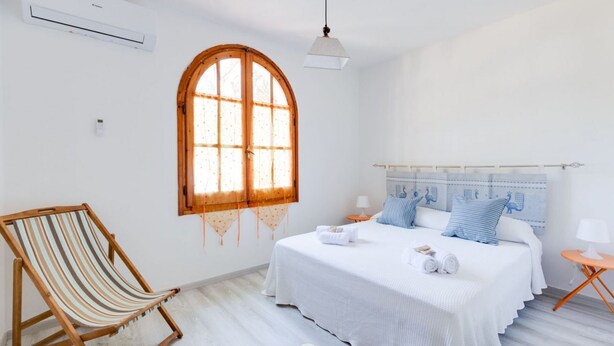 Un dormitorio con cama, ventana, silla y lámpara.