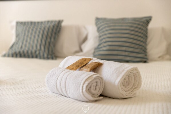 A neatly made white towel with a tag on a bed with striped pillows.