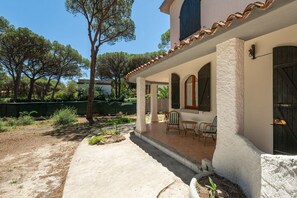 Ein Haus mit überdachter Terrasse, Sitzgelegenheit im Freien und einem Garten.