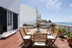 Eine Terrasse mit rundem Tisch und Stühlen, einer Topfpflanze und Blick aufs Meer.
